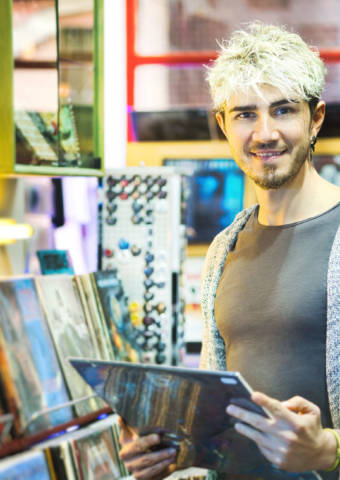 Young Man Browsing Through Vintage Discs and Choosing Vinyl LP In Records Shop. Portrait of Customer Smiling At Camera And Buying Music Albums.