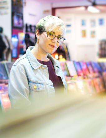 Young Woman Browsing Through Vintage Discs and Choosing Vinyl LP In Records Shop. Portrait of Customer Smiling At Camera And Buying Music Albums.