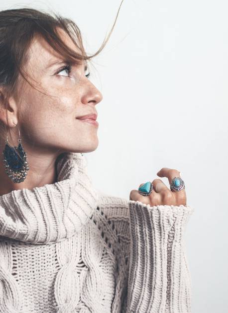 Boho jewelry on model: ethnic stone rings and earrings. Beautiful woman wearing warm woolen sweater and fashion jewellery. Minimal style and pastel tone.